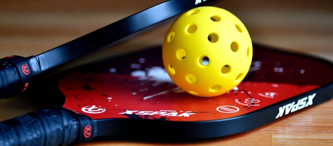 Pickleball paddle and yellow ball on a court, ideal for Houston pickleball courts and enthusiasts.
