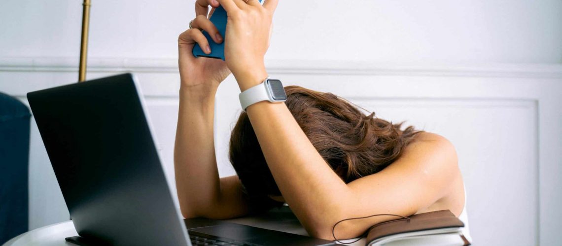 Frustrated HOA board member overwhelmed with phone and laptop.