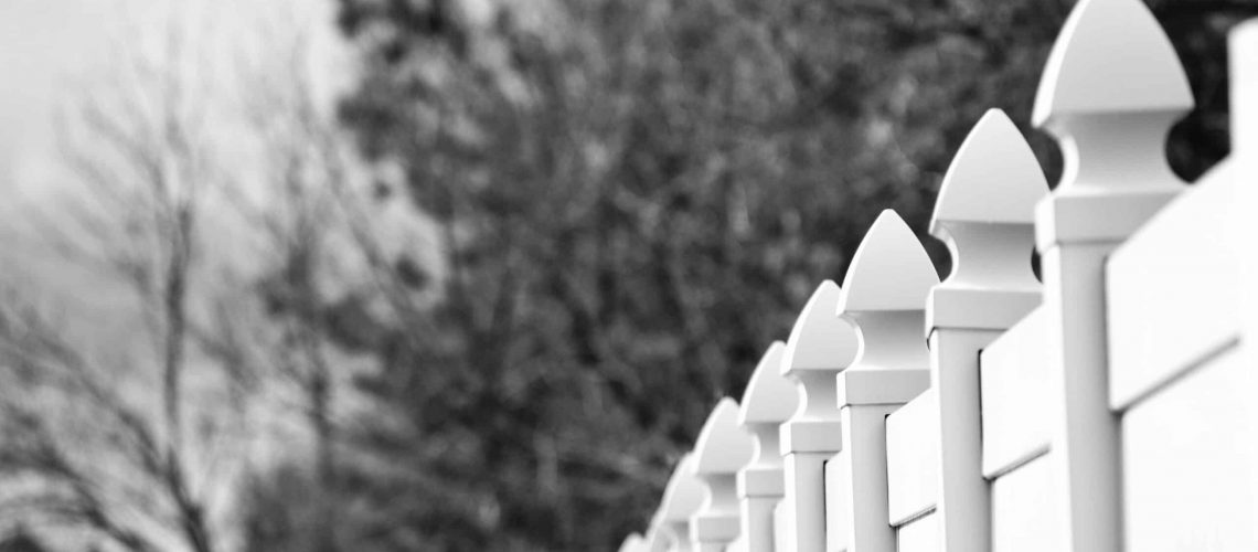 White picket fence with trees in background, illustrating HOA conflicts.