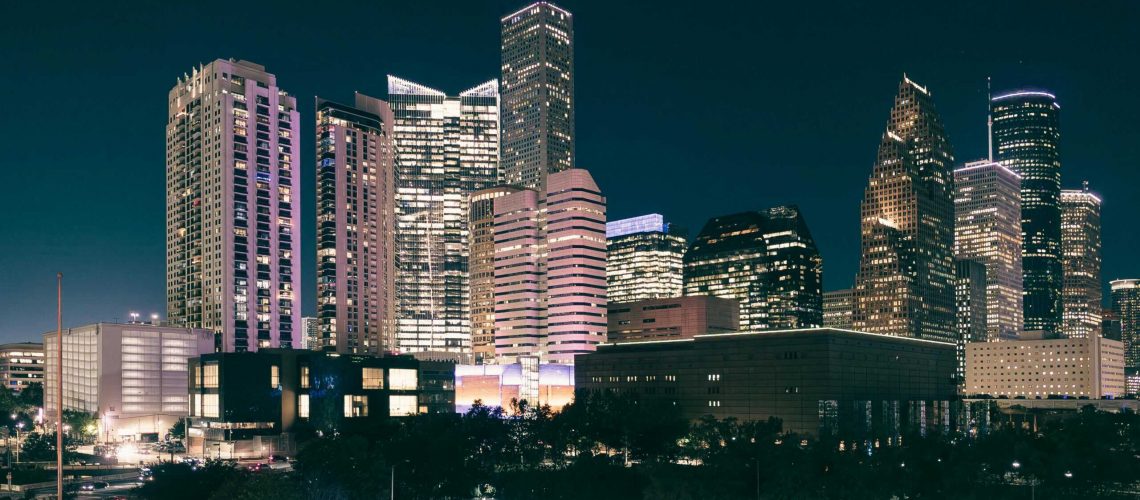 City skyline at night with illuminated skyscrapers and office buildings.