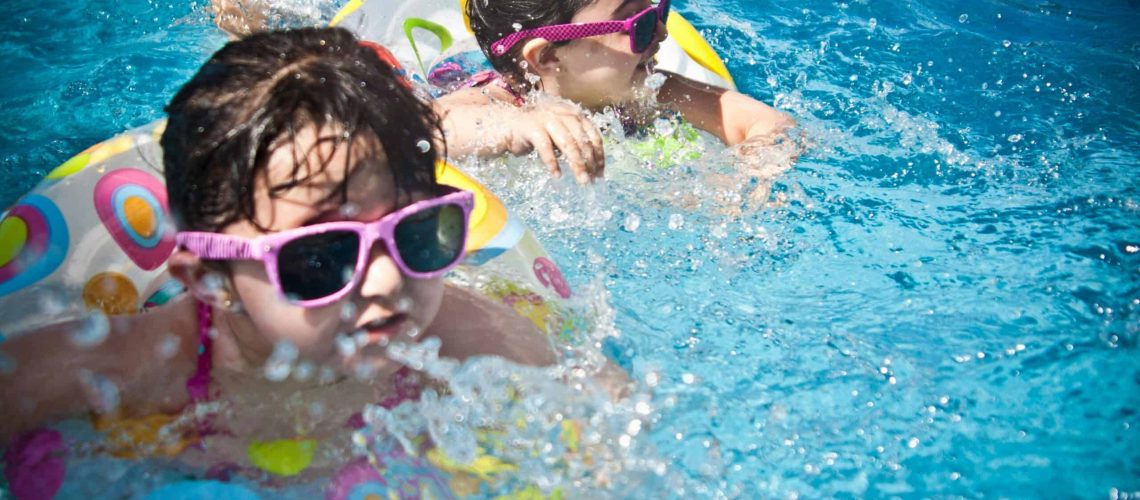 Kids enjoying swimming in a pool with floaties and sunglasses during summer.