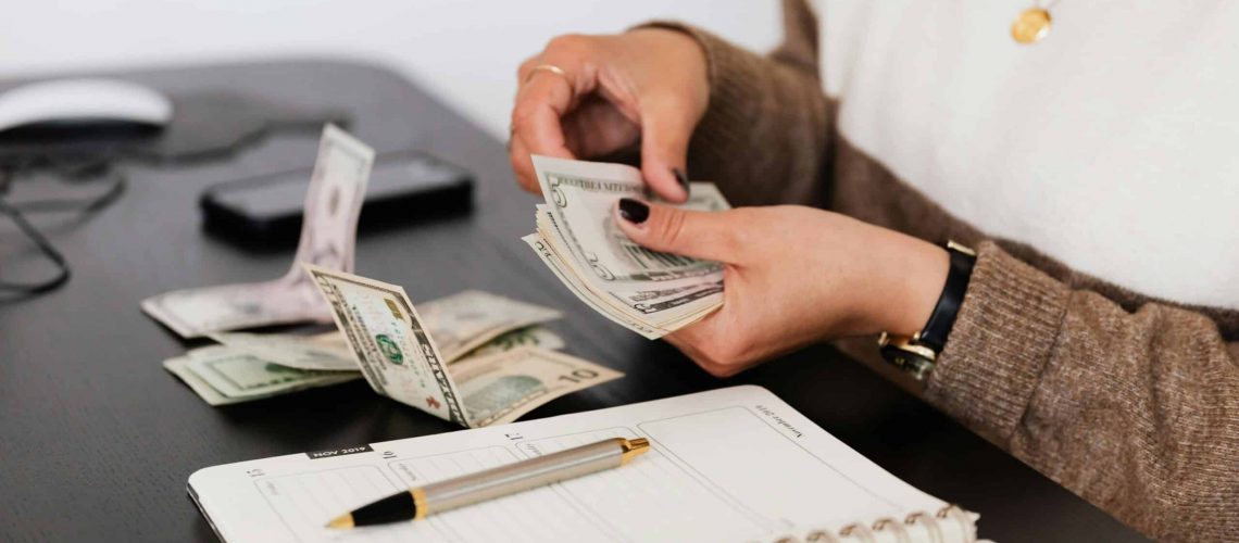 Woman counting money with a notebook and pen on a desk.