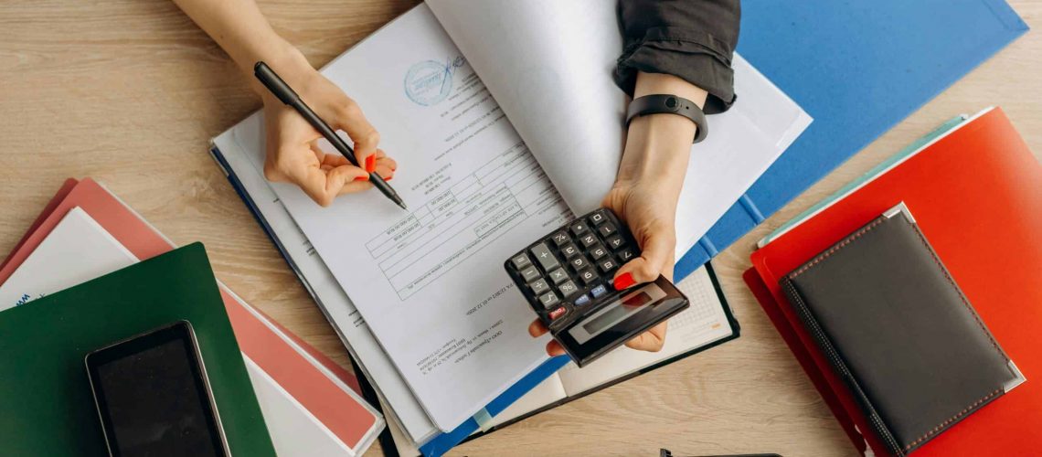 Person working with financial documents and calculator on a desk.