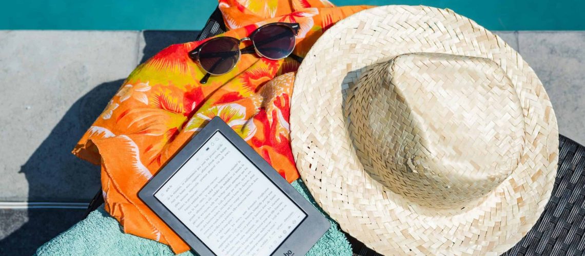 Sun hat, sunglasses, and e-reader on a poolside lounge chair.