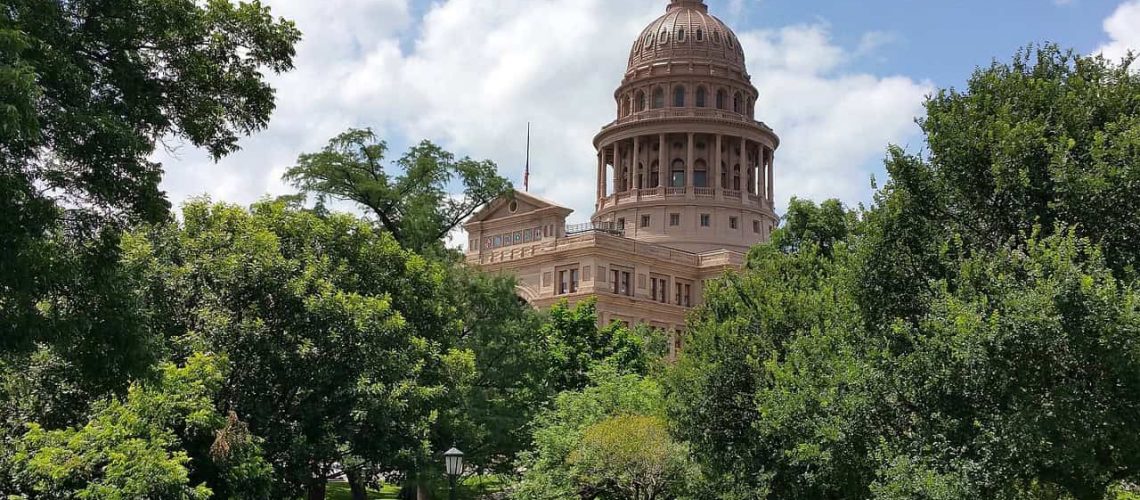 Texas Capitol with lush greenery and blue sky, symbolizing legislative progress.
